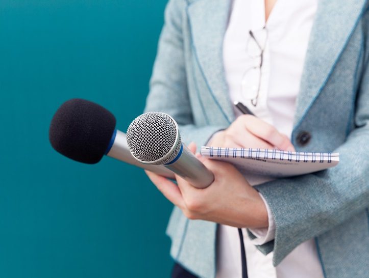 Reporter or TV journalist at news conference, holding microphone and writing notes